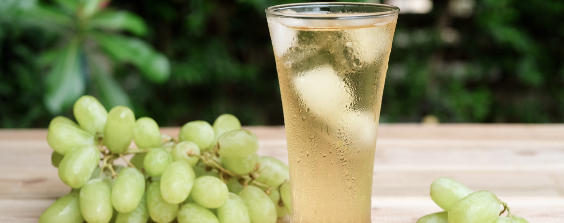 Kalter Traubensaft im Glas mit Eiswürfeln, umgeben von frischen grünen Trauben.