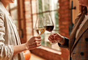 Zwei Personen prosten mit Rot- und Weißweingläsern in eleganter Umgebung an.