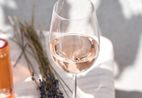 Weinglas mit Roséwein neben Lavendel auf Leinentuch.