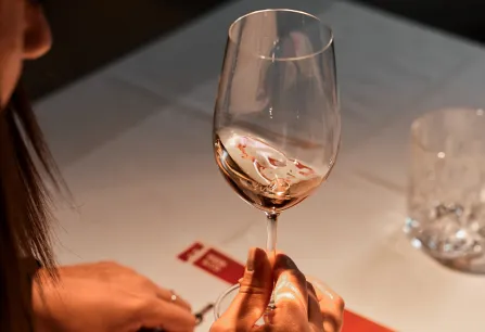 Person hält Weinglas über Tisch mit untergelegtem Papier.