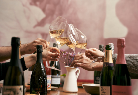 Personen stoßen mit Weißweingläsern an, umgeben von Champagnerflaschen.