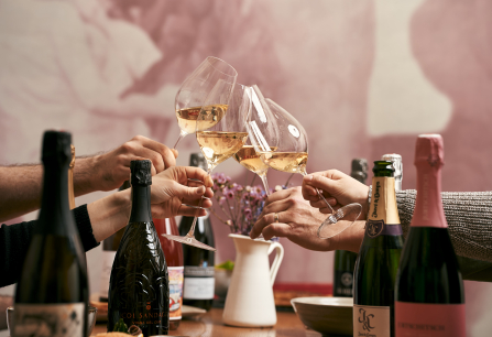 Personen stoßen mit Weißweingläsern an, umgeben von Champagnerflaschen.