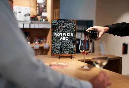 Person schenkt Rotwein in Glas, Flasche und Weingläser auf Holztheke.