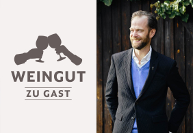 Ein Mann im Anzug lächelnd, vor dunklem Holzhintergrund.