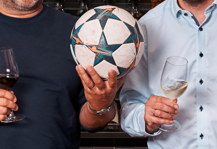 Zwei Männer halten Weingläser und einen Fußball.