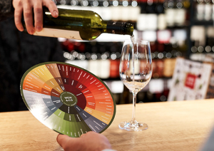 Person schenkt Wein in Glas mit Farbkreis in moderner Weinhandlung ein.