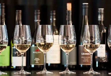 Sechs Weingläser vor einer Reihe von Weinflaschen auf dunklem Hintergrund.