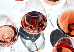 Mehrere Weingläser mit Roséwein auf weißem Hintergrund, elegante Licht- und Schatteneffekte.