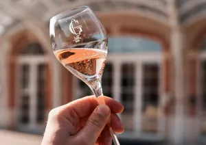 Hand hält Sektglas mit roséfarbenem Getränk vor elegantem Gebäude.