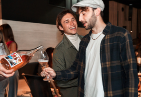 Zwei Männer lachen und stoßen mit einem Glas Roséwein an.