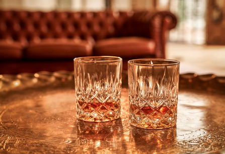 Zwei verzierte Whiskygläser auf einem eleganten Metalltablett vor Ledersofa.