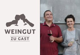 Mann und Frau halten Weingläser, lächelnd vor einer Tafel stehend.