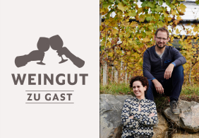 Mann und Frau sitzen lächelnd vor herbstlichen Reben im Weinberg.
