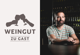 Mann in gestreiftem Shirt sitzt an einem Tisch, Weinflaschen im Hintergrund.