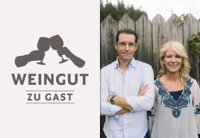 Mann und Frau vor Holzzaun, links Weingut-Logo mit Gläsern.