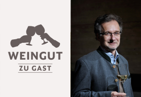 Mann im traditionellen Anzug hält Weinglas, dunkler Hintergrund.