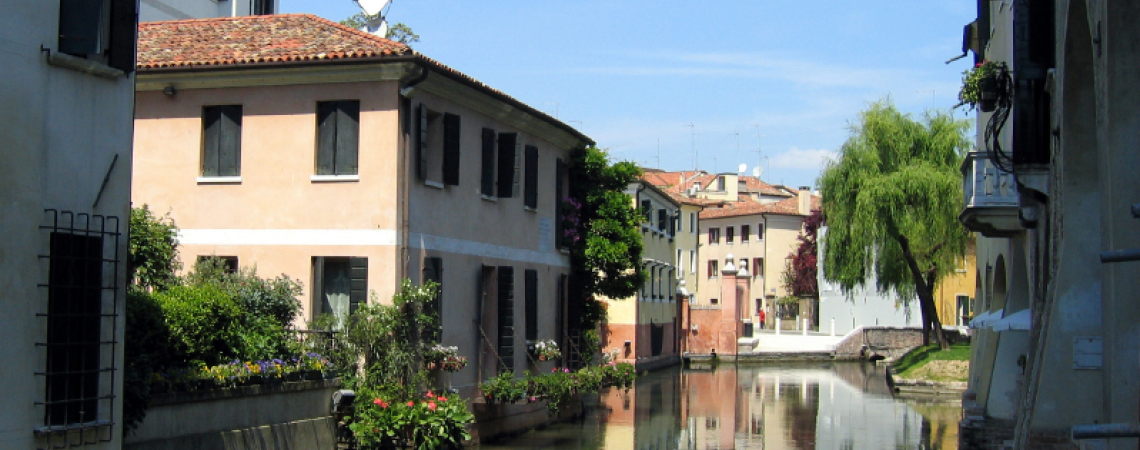 Malersichene Wasserstraße mit bunten Häusern und üppigem Grün unter blauem Himmel.