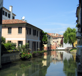 Malersichene Wasserstraße mit bunten Häusern und üppigem Grün unter blauem Himmel.