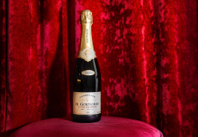 Champagnerflasche auf rosa Samthocker vor rotem Samthintergrund.