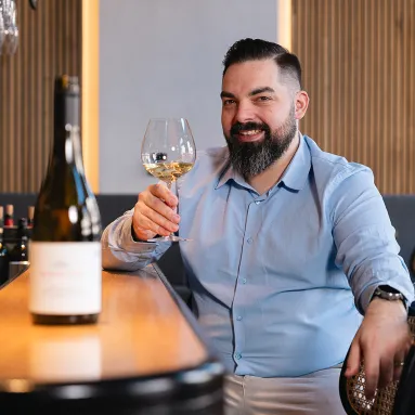 Mann in blauem Hemd genießt Glas Weißwein an einer stilvollen Bar.