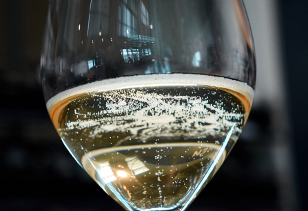 Nahaufnahme eines Champagnerglases mit sprudelndem Sekt vor unscharfem Hintergrund.