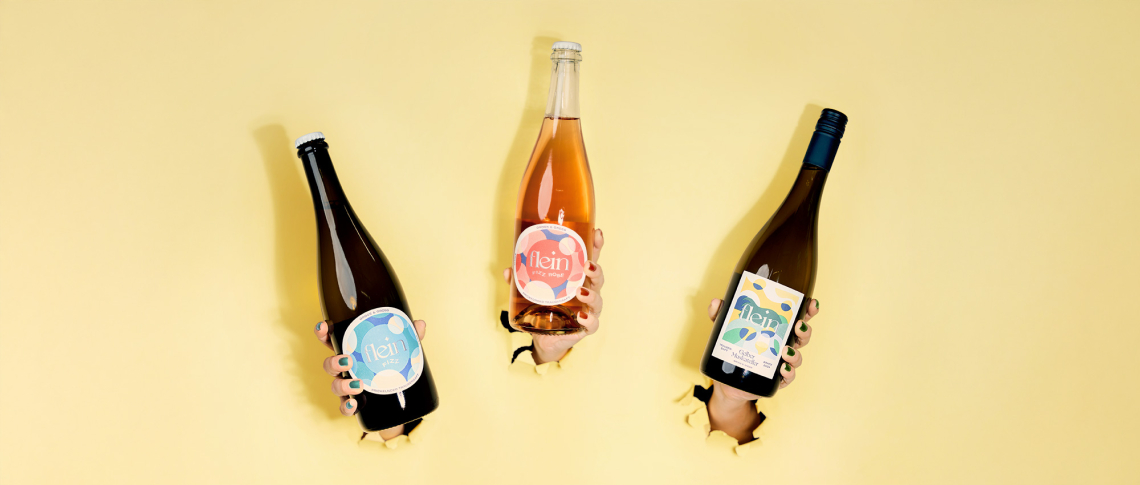 Drei Weinflaschen in Händen vor gelbem Hintergrund durchbrechen Papier.