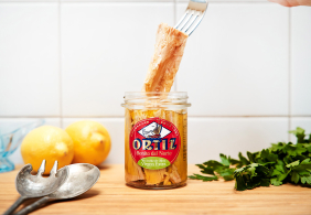 Glas mit Thunfischfilets, umgeben von Zitronen, Besteck und Kräutern.