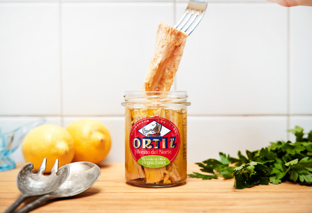 Glas mit Thunfischfilets, umgeben von Zitronen, Besteck und Kräutern.