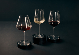 Drei Weingläser mit Rot- und Weißwein auf dunklem Hintergrund, stilvoll präsentiert.