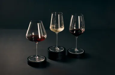 Drei Weingläser mit Rot- und Weißwein auf dunklem Hintergrund, stilvoll präsentiert.