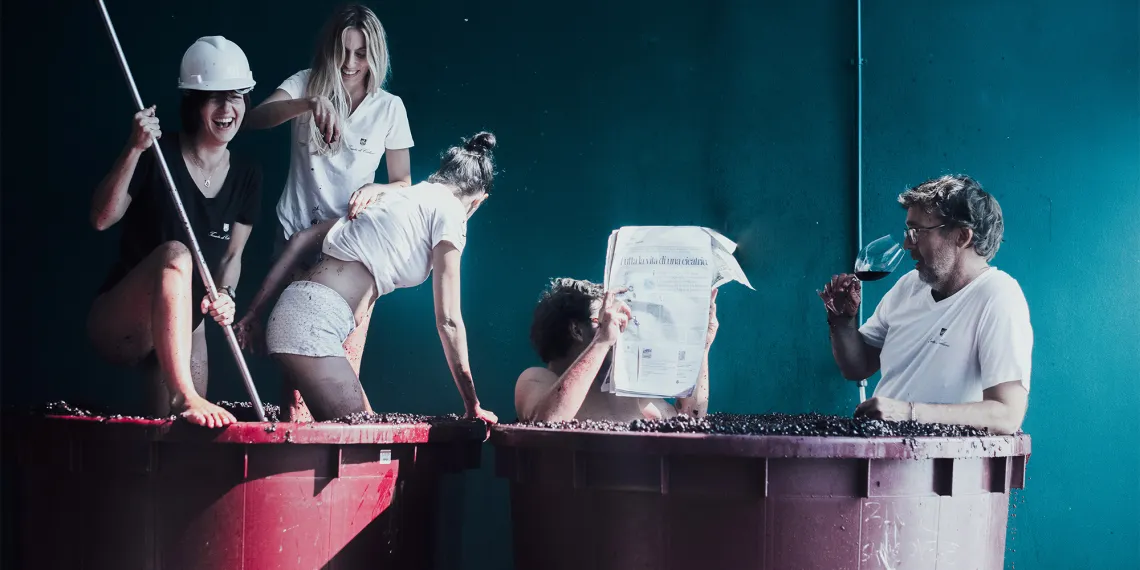 Gruppe von Menschen in großen Weinfässern, teils lesend, teils Wein trinkend.