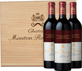 Drei Rotweinflaschen vor einer Holzkiste mit elegantem Wappen.