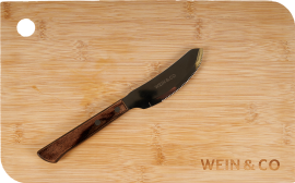 Ein gezacktes Messer mit dunklem Holzgriff liegt auf einem hellen Bambus-Schneidebrett. Oben links befindet sich eine runde Aussparung im Brett.