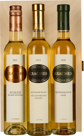 Drei elegante Weinflaschen in einer Holzkiste, jeweils mit unterschiedlichen goldenen und grünen Kapseln. Die Etiketten sind in klarer, klassischer Schrift gestaltet mit zentralen Logo-Emblemen. Die Flaschen enthalten goldgelben Wein und strahlen eine hoc