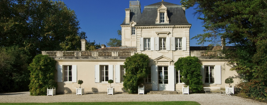 Helles, klassisches Herrenhaus mit französischer Flagge und gepflegtem Garten.