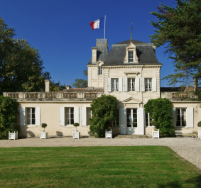 Helles, klassisches Herrenhaus mit französischer Flagge und gepflegtem Garten.