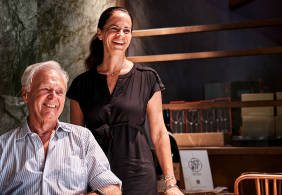 Zwei lachende Personen in einem stilvollen, modern eingerichteten Raum mit Holzmöbeln.