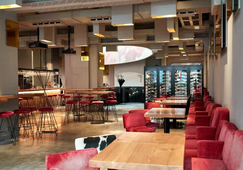 Moderne Restaurant-Inneneinrichtung mit roten Samtstühlen, Holztischen und großzügiger Weinpräsentation.
