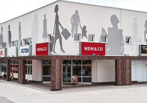 Modernes Einkaufszentrum mit großen Schattensilhouetten an der Fassade.