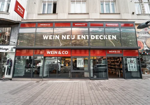 Moderne Fassade eines Weinladens mit großen Glasfenstern und rotem Logo-Element.
