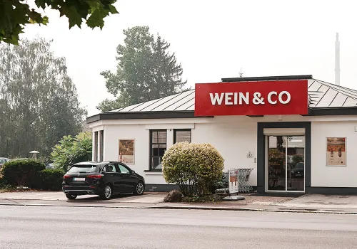 Kleines weißes Gebäude mit rotem Schild und geparktem Auto davor.