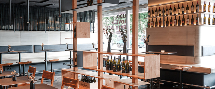 Modernes Restaurant-Interieur mit Holzregalen, Tischen und dekorativen Weinflaschen.