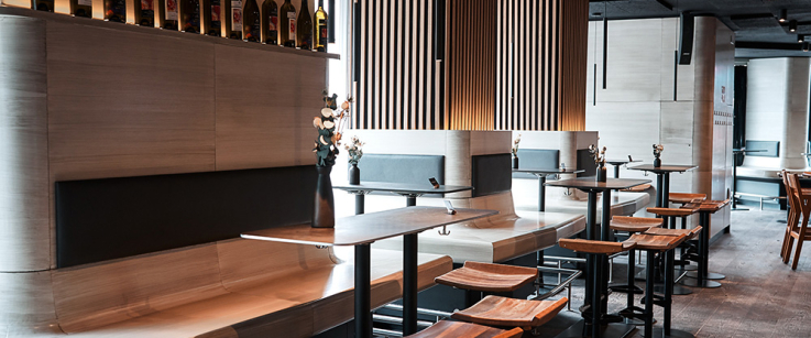 Moderne Bistro-Einrichtung mit Holzhockern und beleuchteten Weinregalen an der Wand.