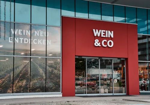 Moderne Fassade eines Weinladens mit Glasfront und rotem Eingangsbereich.
