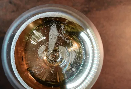 Schräg von oben fotografiertes Bierglas auf dunkler Tischoberfläche.