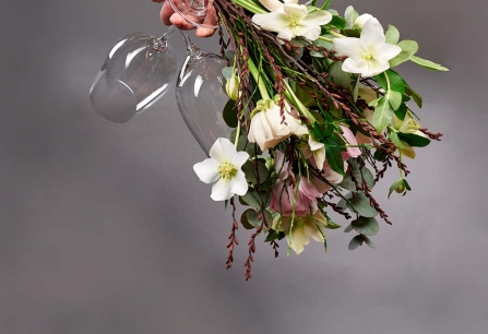 Blumenstrauß mit weißen Blüten und Weingläsern, auf grauem Hintergrund.