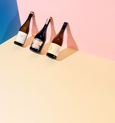 Drei Weinflaschen auf farbigem Hintergrund in Blau, Rosa und Beige.