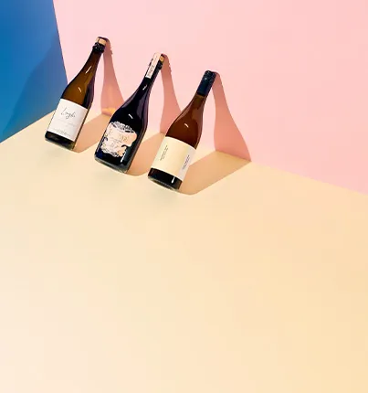 Drei Weinflaschen auf farbigem Hintergrund in Blau, Rosa und Beige.