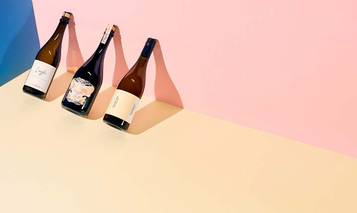 Drei Weinflaschen auf farbigem, minimalistischem Hintergrund.