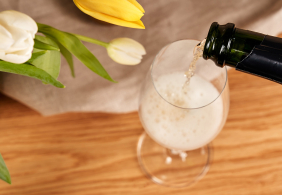 Sekt wird in ein Glas gegossen, daneben gelbe und weiße Tulpen.